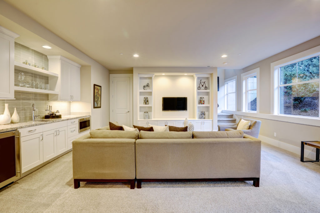 Chic basement features a gray sectional facing a white built-in tv cabinet and wet bar mounted to a wall